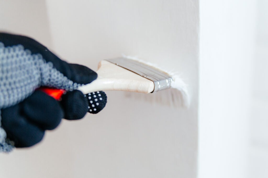 Close-up of a worker's hand with a brush painting a wall with white paint. Painting apartment, renovating with white color paint.