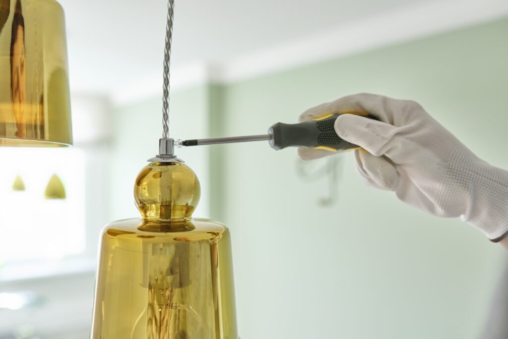 Hands with screwdriver fitting installing lamp, chandelier, closeup.