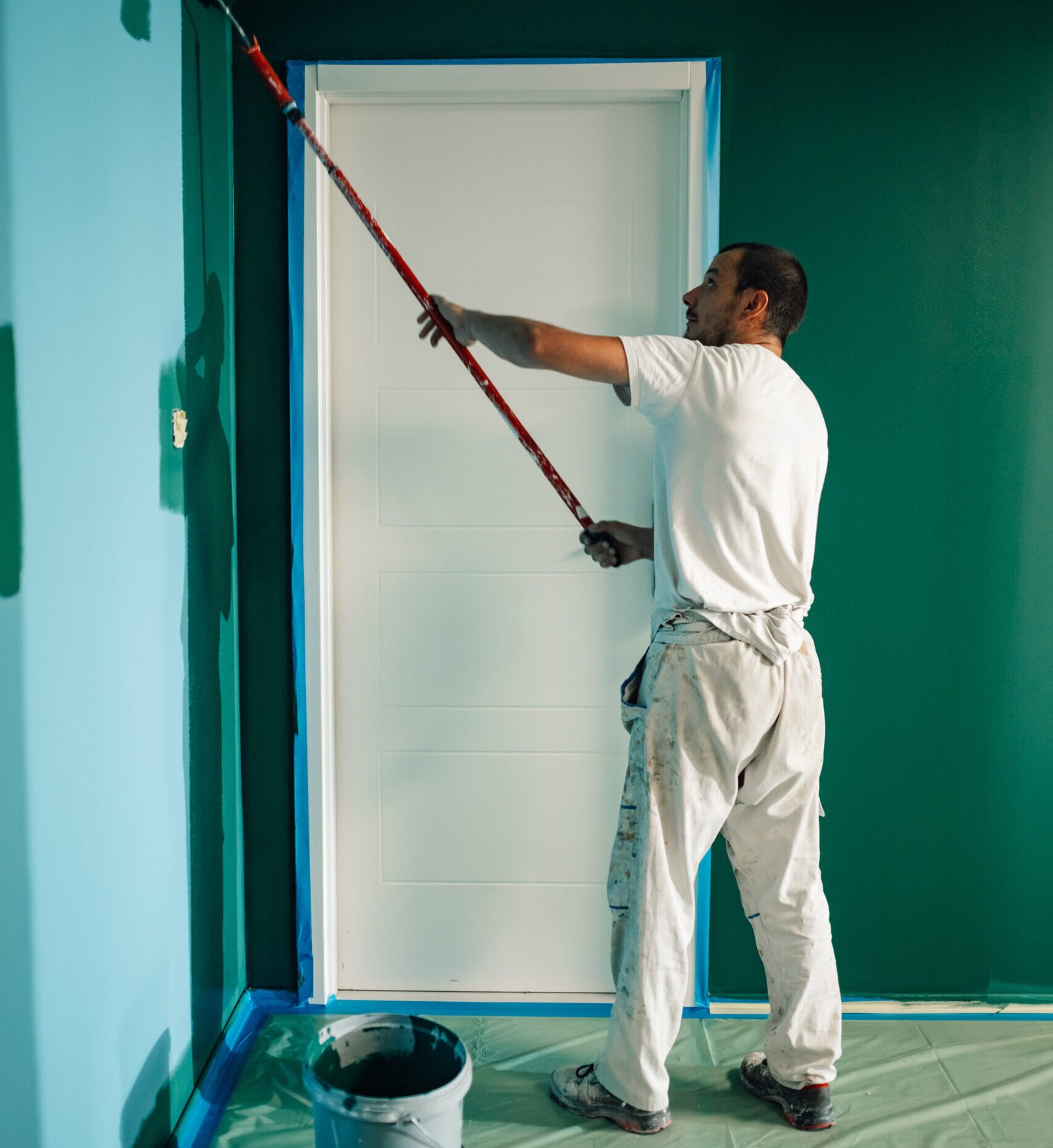 Professional painter using a telescopic paint roller painting a wall green in a house during renovation works