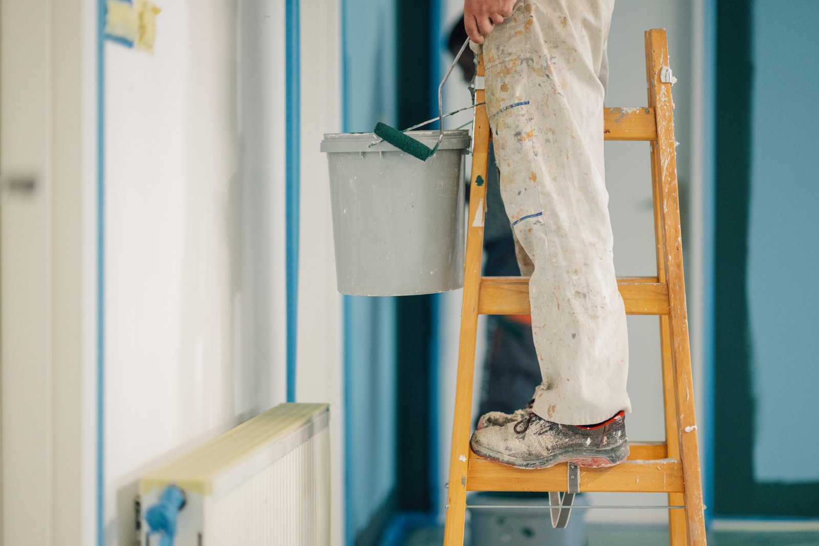 House painter standing on a wooden ladder, holding a paint bucket, working on renovations in a residential property