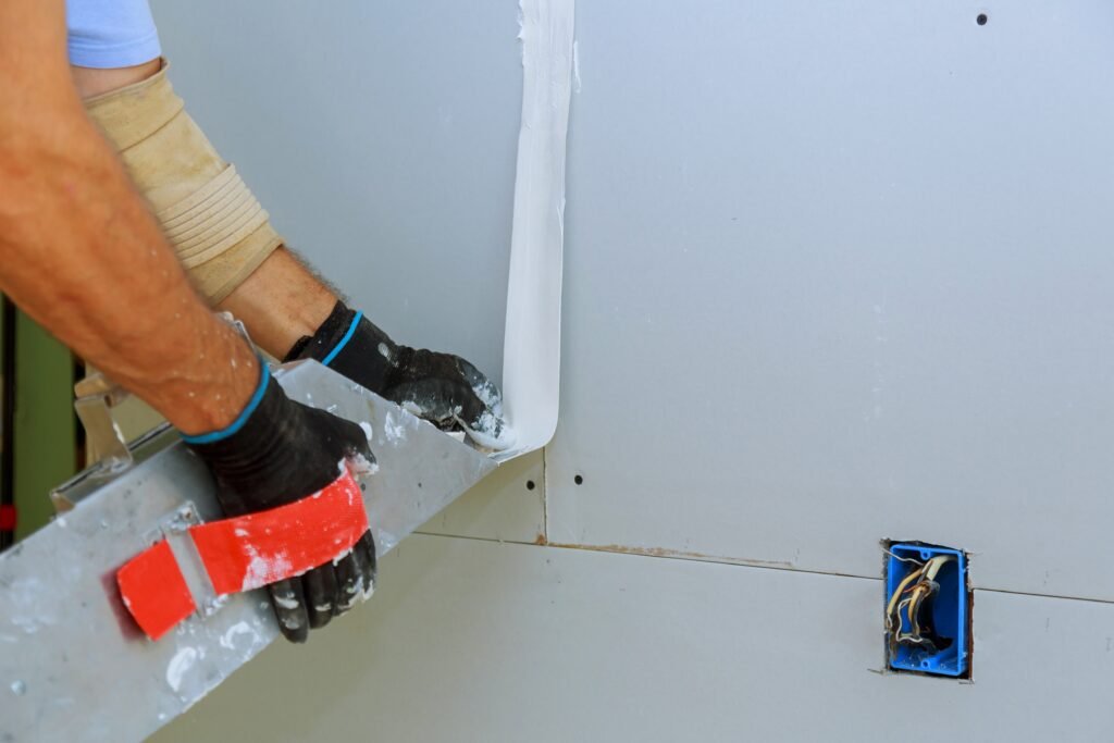 Worker installing gypsum board to wall interior of a room under construction